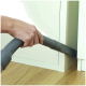 Eine Hand, die einen Staubsaugerschlauch hält und in einen engen Raum zwischen einem Schrank und dem Boden greift, auf einem Holzboden.