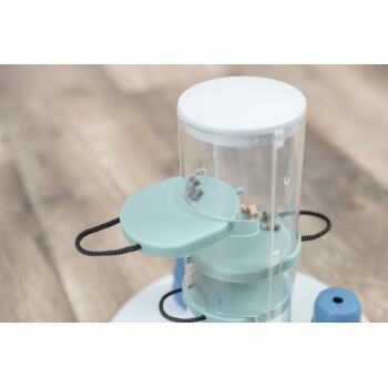 Automatyczny podajnik karmy dla zwierząt wydający suchą karmę, z przezroczystym pojemnikiem i niebieską podstawą na drewnianej podłodze.