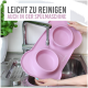 Eine Person hält eine rosa Silikon-Haustierfütterungsmatte mit zwei Schalen über einem Waschbecken mit fließendem Wasser. Text: "Einfach zu reinigen, spülmaschinenfest."