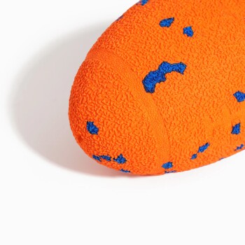 Nahaufnahme eines eiförmigen orangefarbenen, strukturierten Hundekauspielzeugs mit blauen Punkten auf weißem Hintergrund.