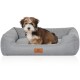 Ein kleiner, flauschiger Hund sitzt bequem in einem grauen Haustierbett mit einem Lederanhänger, auf dem "KNUFFELWUFF" steht.
