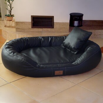 Schwarzes Leder-oval Haustierbett mit erhöhten Rändern und passendem Kissen auf gefliestem Boden in häuslicher Umgebung.