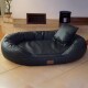 Schwarzes Leder-oval Haustierbett mit erhöhten Rändern und passendem Kissen auf gefliestem Boden in häuslicher Umgebung.