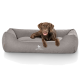 Ein brauner Hund, der auf einem gemütlichen grauen Hundebett mit dem Logo "KNUFFELWUFF" sitzt, das prominent auf der Vorderseite angezeigt wird.
