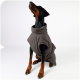 Ein brauner und schwarzer Hund trägt einen weichen, grauen Haustiermantel, von hinten gegen einen schlichten weißen Hintergrund betrachtet.