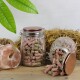 Glasbehälter mit rosa und grünen Tierpellets, einer stehend und einer verschüttet auf Holz, mit Heu, Salzstein und Blättern