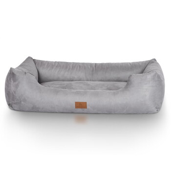 Ein brauner Hund ruht sich bequem in einem weichen, grauen Hundebett mit einem Lederetikett aus, das ein gemütliches und einladendes Design zeigt.