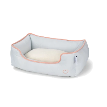 Lit pour animaux de compagnie bleu clair avec un coussin blanc doux, présentant une bordure rose et un petit logo en forme de cœur sur le côté.