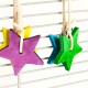 Bunte, sternförmige Haustierspielzeuge aus Holz in Lila, Gelb, Blau und Grün, die an einem Drahtkäfig hängen.
