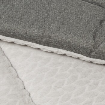 Eine Nahaufnahme eines Haustierbettes mit einer weichen, plüschigen weißen Unterseite mit einem strukturierten Muster und einer grauen Stoffoberfläche.