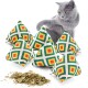 Eine graue Katze spielt mit sechs bunten pyramidenförmigen Katzenminze-Spielzeugen, mit getrockneter Katzenminze, die davor verstreut ist.