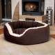 Braun-beiges, rundes Plüsch-Haustierbett auf gefliestem Boden vor einem beleuchteten Kamin in einem gemütlichen Raum.