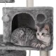 Eine graue getigerte Katze liegt in einem plüschigen Katzenbaum mit einer gemütlichen Höhle und einem baumelnden Pom-Pom-Spielzeug.