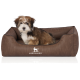 Ein kleiner, flauschiger Welpe mit braunem und weißem Fell sitzt bequem in einem braunen Haustierbett, mit dem Logo 'KNUFFELWUFF'.
