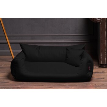 Ein schwarzes Hundebett mit zwei plüschigen Kissen, vor einer dunklen Wand und einem Holzboden, ideal für kleine bis mittelgroße Haustiere.