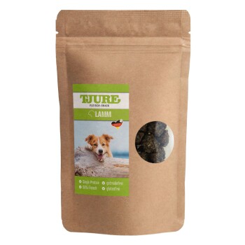 Braune Papiertüte mit "TJURE Fleisch-Snack Lamm" Hundeleckerlis, mit einem glücklichen Hund und Etiketten für "Single Protein," "96% Fleisch," und "glutenfrei."
