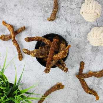 Eine schwarze Schüssel gefüllt mit Hundekauartikeln aus getrockneten Fleischstangen, umgeben von verstreuten Kauartikeln und einer kleinen grünen Pflanze.