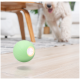 Ein grüner, leuchtender Hundespielzeugball springt auf einem Holzboden, mit einem verspielten Hund im Hintergrund, der eifrig näher kommt.