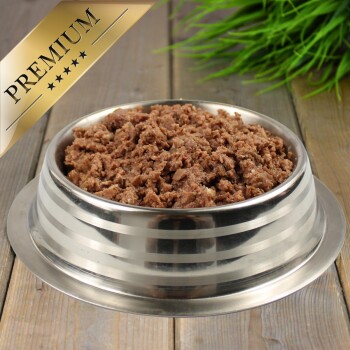 Eine Edelstahlschüssel für Haustierfutter, gefüllt mit hochwertigem Nassfutter für Hunde, mit einer strukturierten, fleischigen Mischung, im Hintergrund grünes Gras.