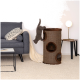 Eine graue Katze springt von einem Kratzbaum mit mehreren Öffnungen, neben einem grauen Sofa mit einem gemusterten Kissen und einer Decke.