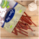 Eine Tüte mit Haustierleckereien, die mit "Lyra Nature Power" gekennzeichnet ist, lässt rote, stangenförmige Leckereien auf eine Holzoberfläche fallen, mit einem weißen Seilspielzeug in der Nähe.