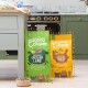 Dwie torby karmy dla psów Edgard Cooper na podłodze kuchni: zielona "Grass-Fed Lamb" i pomarańczowa "Free-Range Turkey & Chicken," z miską na karmę w pobliżu.