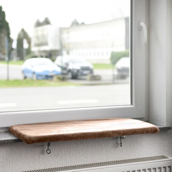 Eine gemütliche Katzenfensterbank mit einem weichen, braunen Kissen, montiert auf einer Fensterbank, mit Blick auf eine Straße mit geparkten Autos.