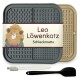 Eine Futtermatte für Haustiere mit der Aufschrift "Leo Löwenkatz Schleckmatte" mit einem Löwendesign, grauen und beigen Farben, plus einer weißen Bürste und einem schwarzen Spatel.