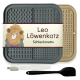 Eine Futtermatte für Haustiere mit der Aufschrift "Leo Löwenkatz Schleckmatte" mit einem Löwendesign, grauen und beigen Farben, plus einer weißen Bürste und einem schwarzen Spatel.