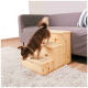 Ein kleiner brauner Chihuahua klettert eine Holzhaustiertreppe hinauf, die zu einem grauen Sofa führt, das auf einem hellen Teppich in einem gemütlichen Wohnzimmer steht.