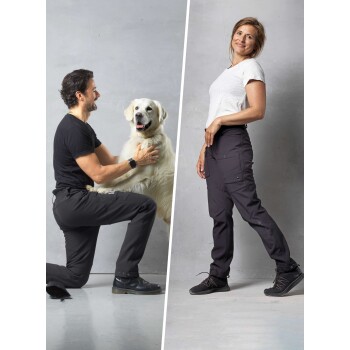 Ein Mann kniet neben einem glücklichen Golden Retriever, während eine Frau selbstbewusst in stylischen schwarzen Hosen steht und tierfreundliche Kleidung präsentiert.