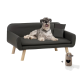 Ein schwarzes Haustiersofa mit Holzbeinen, einem liegenden Hund, einem kleinen Kissen und einem beigen herzförmigen Spielzeug.
