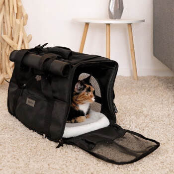 Dreifarbige Katze ruht in einer schwarzen, weichen Transporttasche auf dem Teppich, offene Netzklappe und Markenaufkleber "llonto" sichtbar.