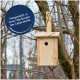 Holz-Vogelhaus, das an einem Baum hängt, mit einem runden Etikett mit der Aufschrift "Hergestellt in einer Werkstatt der Lebenshilfe."