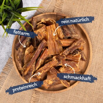 Eine Holzschüssel mit Hundeleckerlis, beschriftet mit "fettarm", "rein natürlich", "proteinreich" und "schmackhaft", mit einer kleinen grünen Pflanze im Hintergrund.