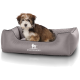 Ein kleiner, flauschiger Hund sitzt bequem in einem grauen Hundebett mit einem gesteppten Innenraum, das das Logo "KNUFFELWUFF" trägt.