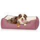 Ein glücklicher Australian Shepherd Hund entspannt sich in einem stilvollen rot-weißen gemusterten Haustierbett mit einem cremefarbenen Innenraum.