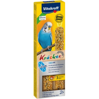 Niebieski papużka na gałęzi obok pudełka Vitakraft Kräcker z 'CALCI-FIT' patyczkami nasiennymi dla zdrowych kości, witamin i bez dodatku cukru.