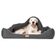Ein großer weißer Hund, der bequem in einem grauen Haustierbett liegt, teilweise mit einer Decke bedeckt, mit einem Holzschild, das "Berendo" beschriftet ist.