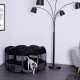 Ein kleiner weißer Welpe mit braunen Flecken verlässt einen schwarzen und grauen Laufstall, hält ein blaues Spielzeug, mit einer Lampe und einem Sofa im Hintergrund.