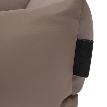 Nahaufnahme eines weichen, beigen Haustierbettes mit einer strukturierten lederähnlichen Oberfläche, mit einem schwarzen Etikett, das den Markennamen geprägt hat.