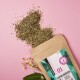 Ein braunes Säckchen mit der Aufschrift "Gastro Kräuter" schüttet Kräuter auf einen rosa Hintergrund, mit kleinen weißen Blumen in der Nähe.