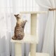 Eine getigerte Katze klettert auf einen mehrstufigen Kratzbaum mit weichen, beigen Oberflächen, in der Nähe von durchsichtigen weißen Vorhängen.