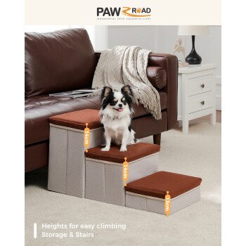 Ein kleiner Hund auf einer dreistufigen Haustiertreppe mit braunen Kissen neben einem Sofa in einem gemütlichen Wohnzimmer. Text: "Höhen für einfaches Klettern, Stauraum & Treppen."