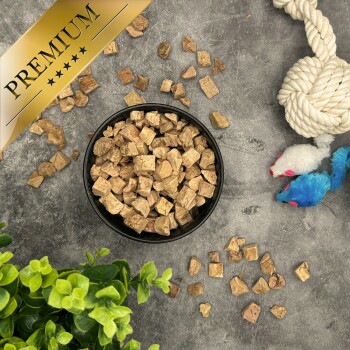 Schwarze Schale mit braunen, gewürfelten Tierleckerlis auf grauer Oberfläche, Spielzeug und Pflanze; goldenes Banner 'PREMIUM'.