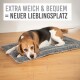 Ein Beagle, der bequem auf einem weichen, grauen Haustierbett liegt, mit dem Text "EXTRA WEICH & BEQUEM = NEUER LIEBLINGSPLATZ" darüber.