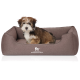 Ein kleiner, flauschiger Hund sitzt bequem in einem braunen Haustierbett mit dem Logo "KNUFFELWUFF" deutlich auf der Vorderseite.