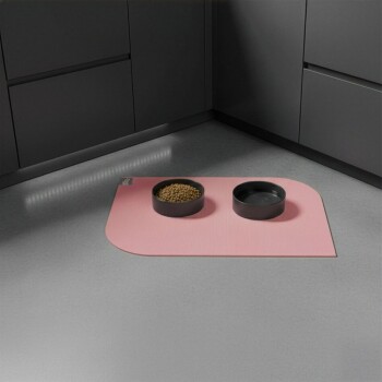 Futternapfstation mit zwei schwarzen Schalen, eine gefüllt mit Trockenfutter, eine leer, auf einer rosa Matte in einer modernen Küche.