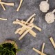 Eine Sammlung von Rinderhaut-Kauspielzeugen, die auf einer grauen Oberfläche verstreut sind, mit zwei geknoteten Seilspielzeugen und einer kleinen Topfpflanze in der Nähe.