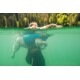 Eine Person in einem Neoprenanzug schwimmt unter Wasser und hält einen Hund in einer blauen Schwimmweste. Das Wasser ist klar grün, mit sichtbaren Blasen.